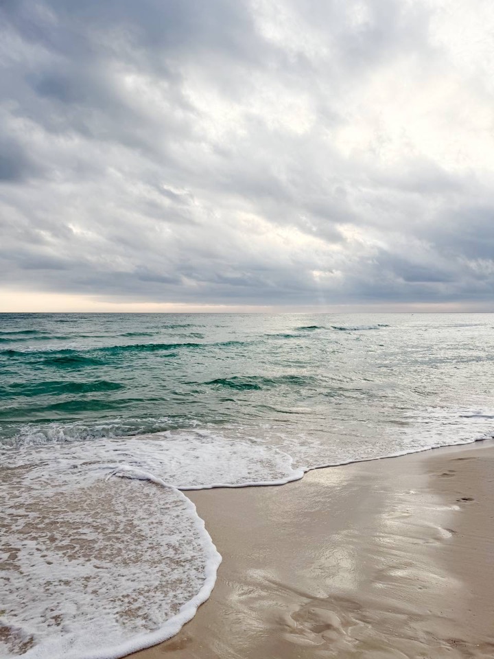 Gentle waves reaching a stretch of pale sand beneath a cloudy sky